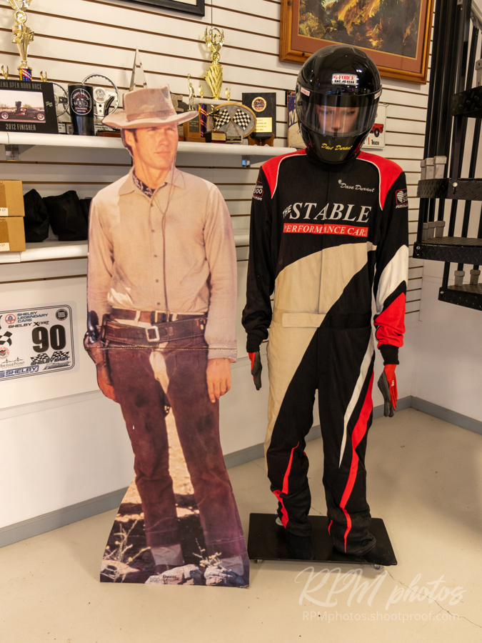 A cutout of Clint Eastwood is displayed next to a mannequin wearing a racing suit for The Stable Performance Cars.