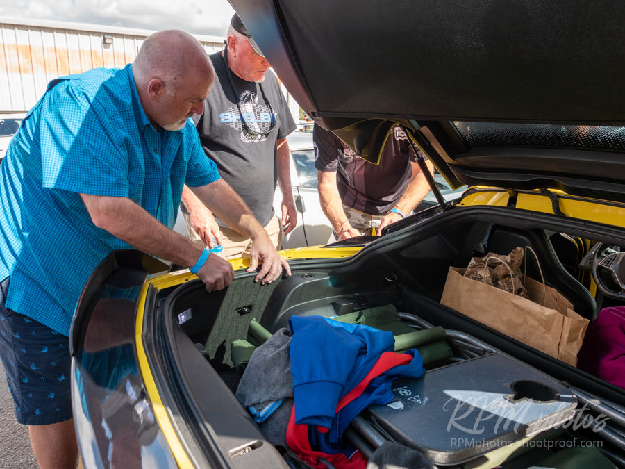 Three men working with a gas cap decal on a yellow car at the car show at The Stable Performance Cars during Octane Fest.