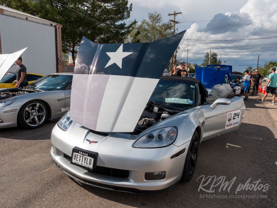 A silver Corvette with a Texas flag on the hood sits in the street during a car show at The Stable Performance Cars during Octane Fest.