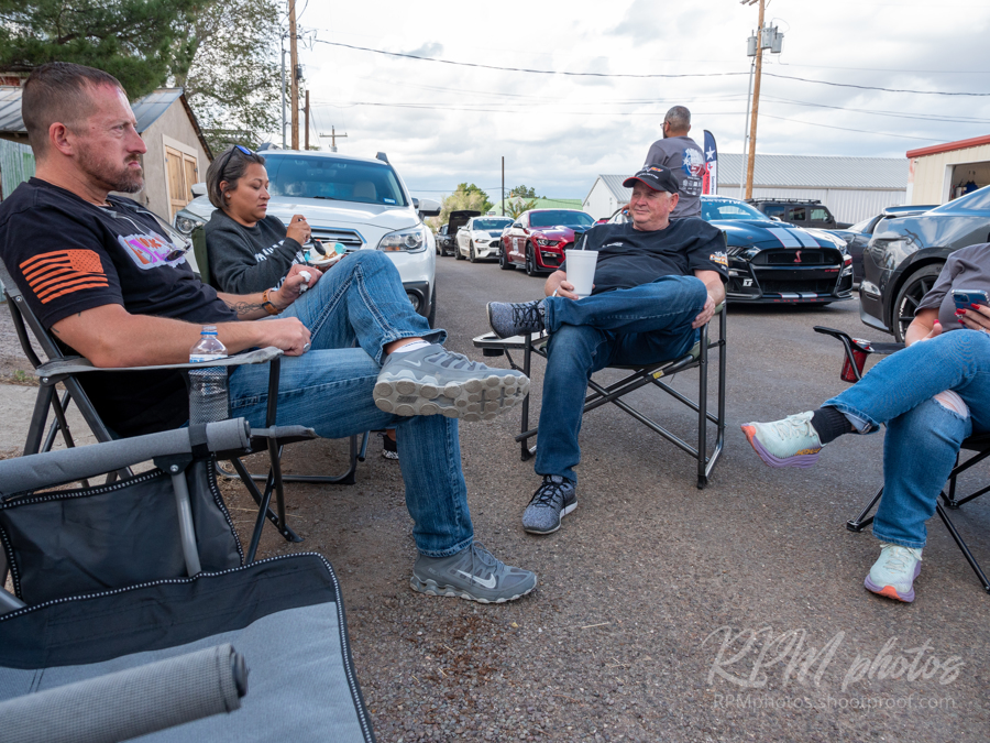 People sit in lawn chairs in the street during a car show at The Stable Performance Cars during Octane Fest.