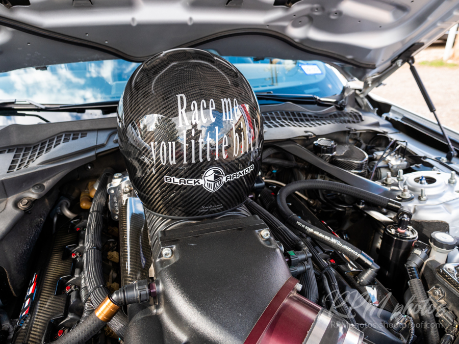 A racing helmet sits in the engine bay of a high performance car, daring others to race, at a car show at The Stable Performance Cars during Octane Fest.