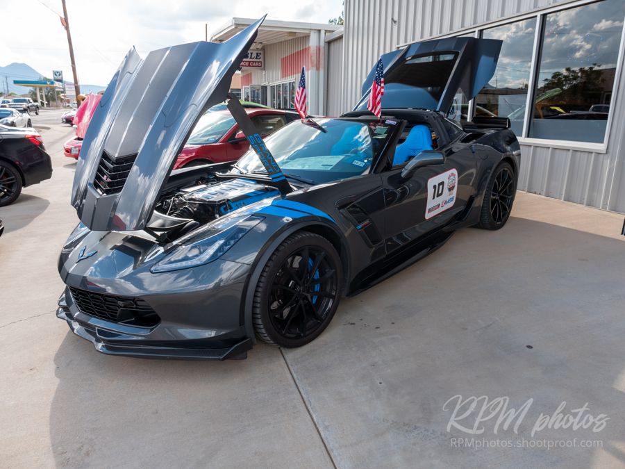 A dark blue Corvette sits with its hood and hatch open in front of The Stable Performance Cars during Octane Fest.