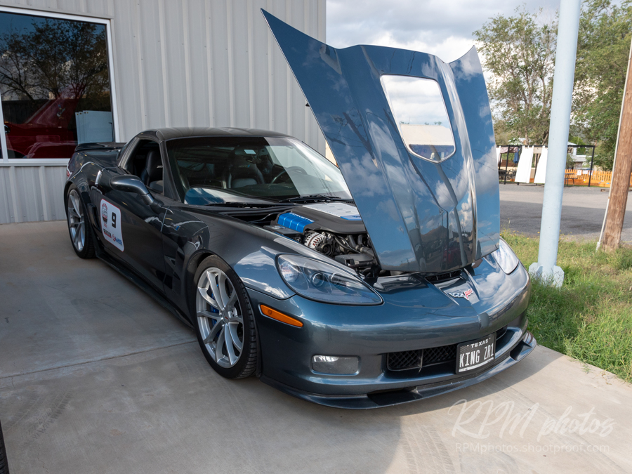 A dark blue Corvette sits with its hood open in front of The Stable Performance Cars during Octane Fest.