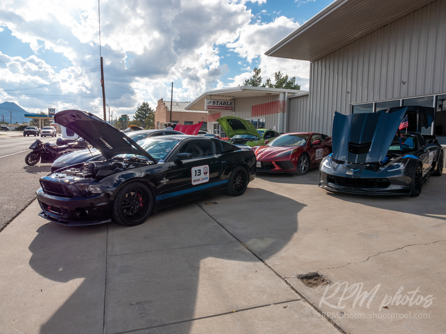 A black Mustang Cobra and a black Corvette parked in front of the The Stable Performance Cars with their hoods open during Octane Fest.
