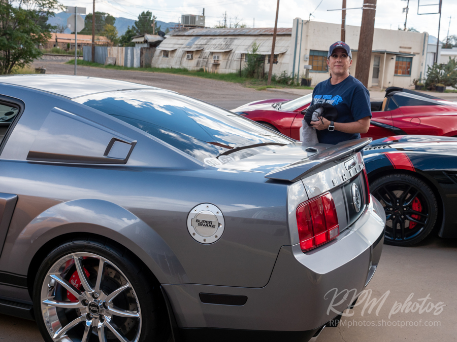 A man stands behind a gray mustang with a "Super Snake" gas cap.